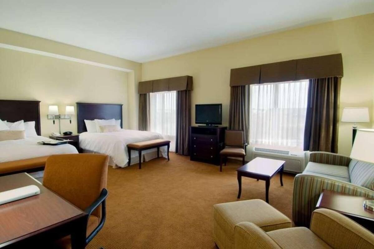 A hotel room with two beds, a TV, a desk, a chair, a sofa, and a small table.