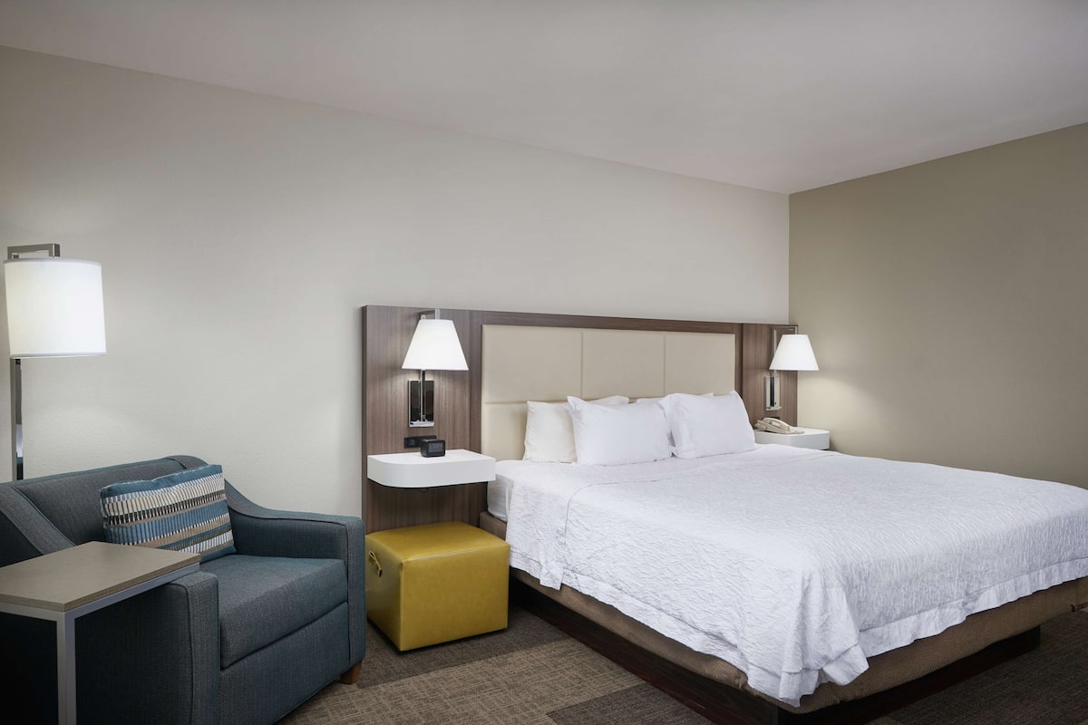 A hotel room with a bed, bedside tables, a sofa, and a small ottoman.