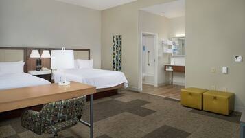 A hotel room with two beds, a desk, a chair, a bathroom, and two storage units.