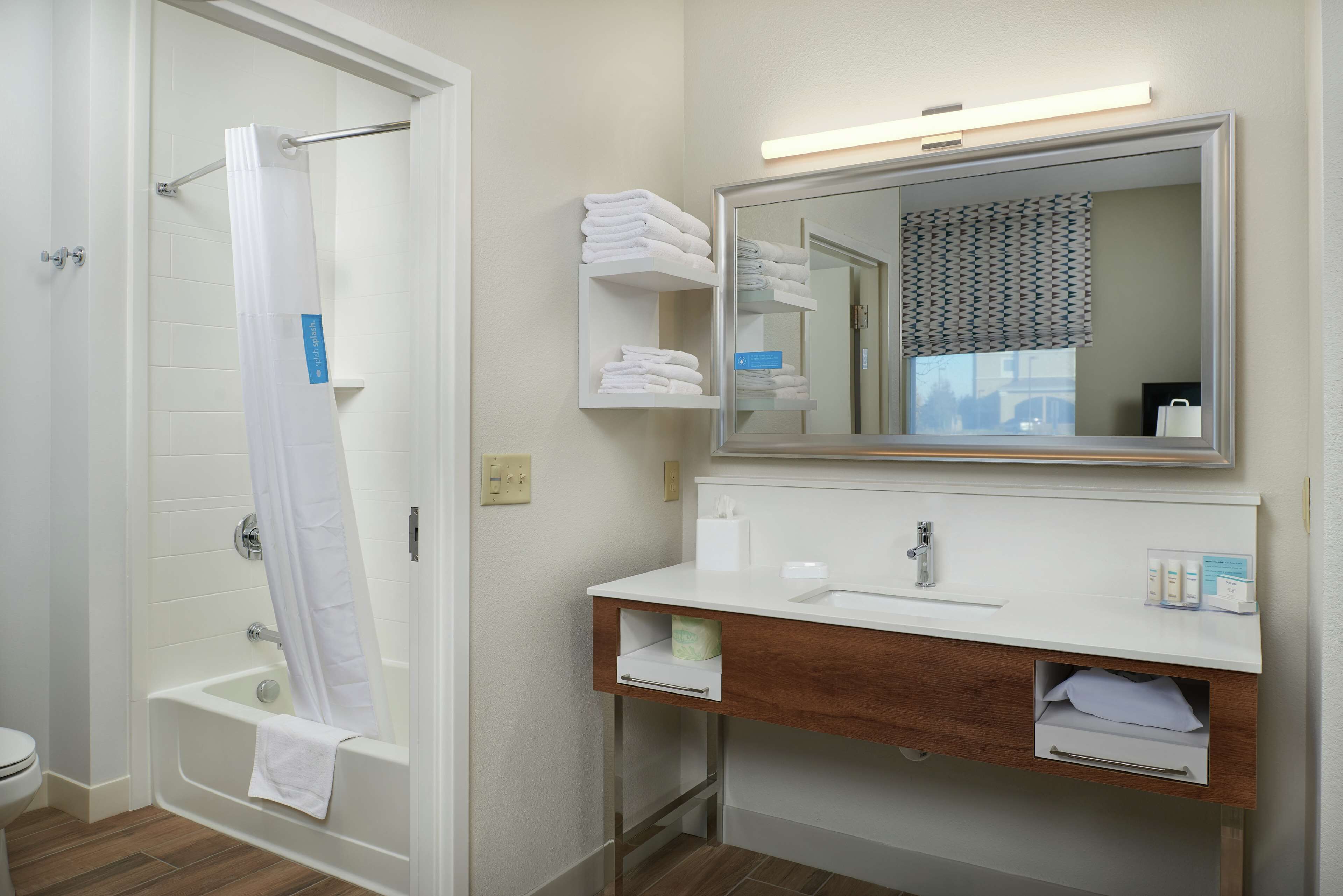 Un baño con bañera, cortina de ducha, lavamanos, espejo y toallero.