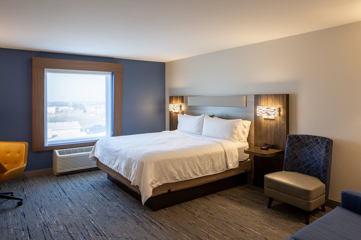 Une chambre d’hôtel avec un grand lit, une chaise, une table de chevet et une fenêtre donnant sur un beau paysage.