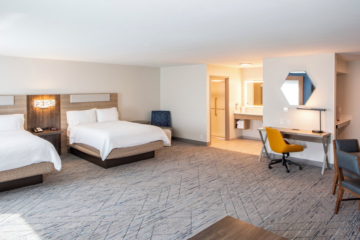 Een hotelkamer met twee bedden, een bureau, een stoel en een badkamer, zichtbaar door een geopende deur.