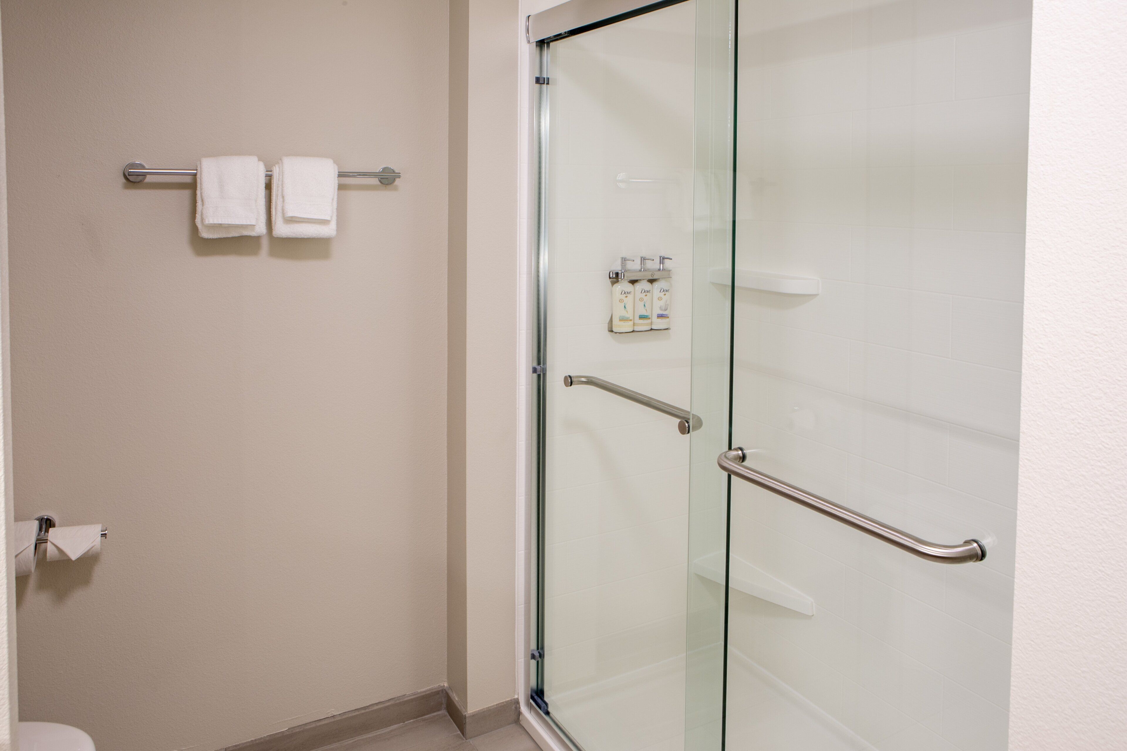 Une salle de bain avec une douche à parois de verre, un porte-serviettes avec deux serviettes et un distributeur de savon fixé au mur.