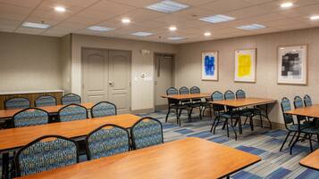 Une salle de conférence avec plusieurs tables et chaises, une porte et des œuvres d’art encadrées accrochées au mur.