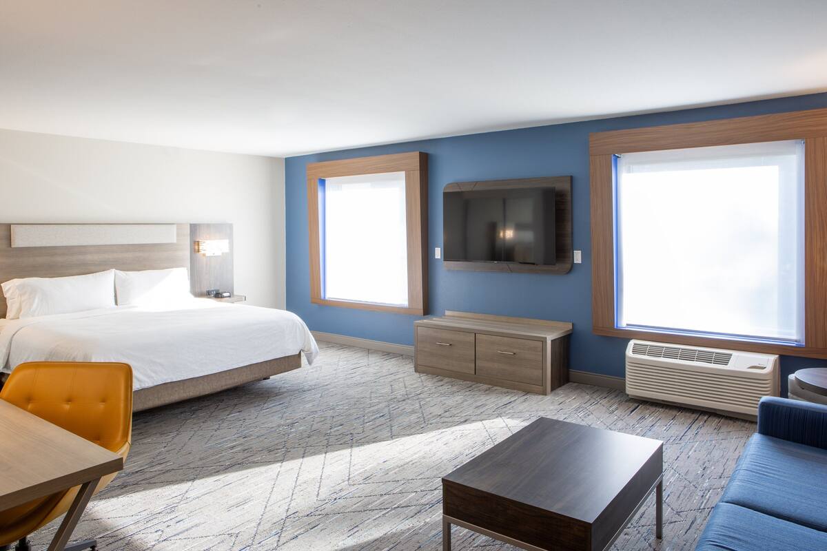 Une chambre d’hôtel équipée d’un lit, d’un téléviseur fixé au mur, d’un canapé, d’une table basse et d’une fenêtre laissant entrer la lumière naturelle.