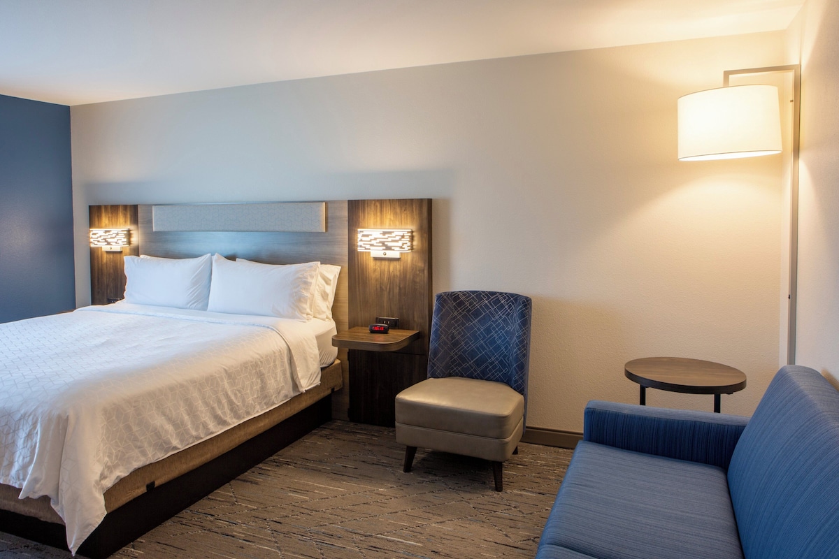 Een hotelkamer met een bed, een stoel, een bank, een nachtkastje en een lamp.