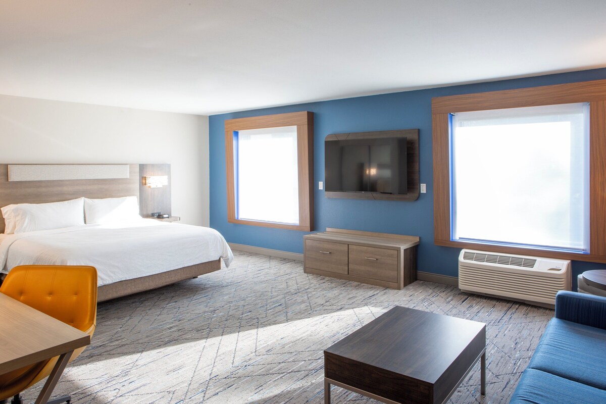Hotelkamer met een bed, een aan de muur bevestigde televisie, een bank, een salontafel en een raam dat natuurlijk licht binnenlaat.