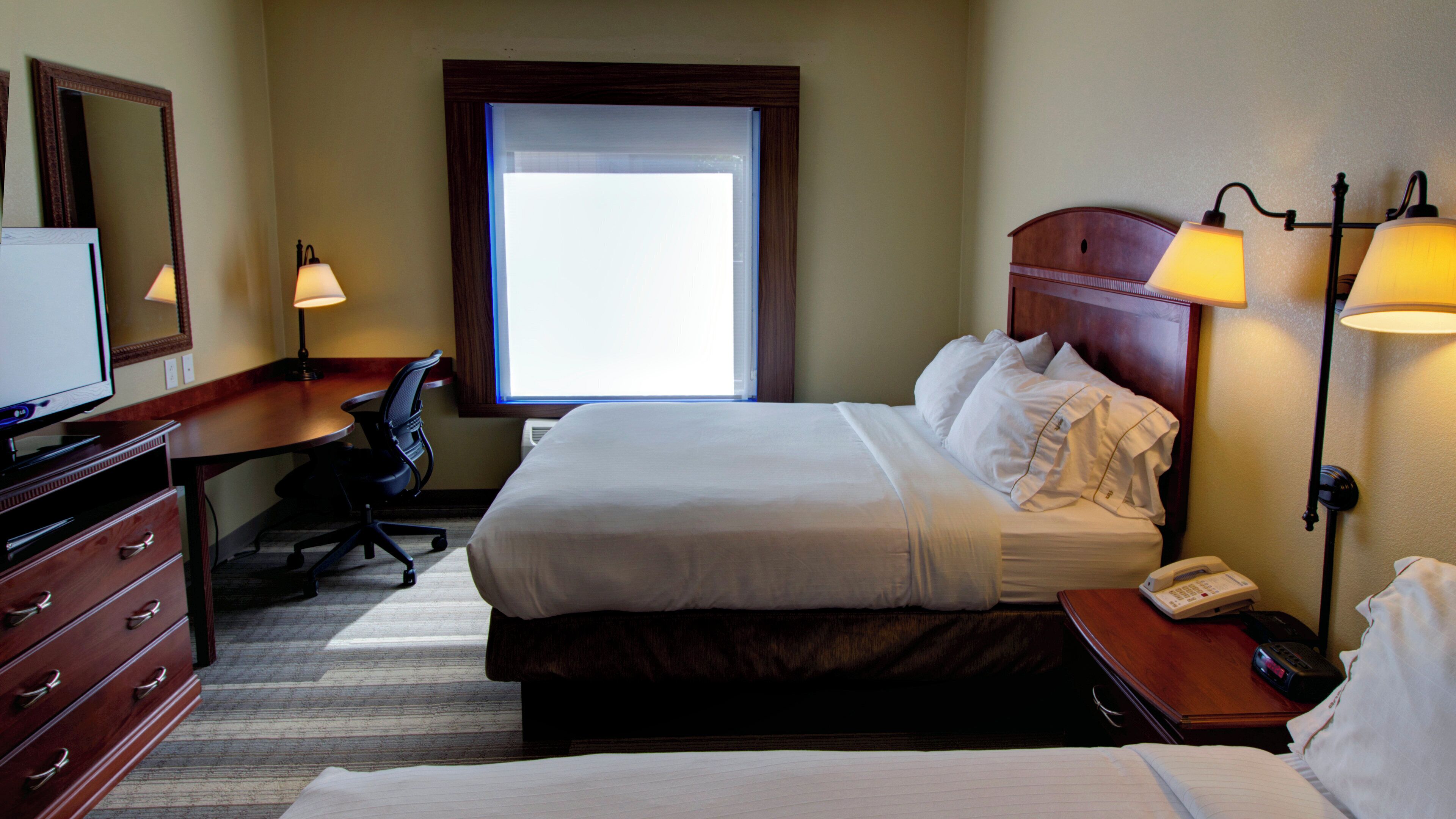 A hotel room with a bed, bedside lamps, a desk with a chair, a television, and a telephone.