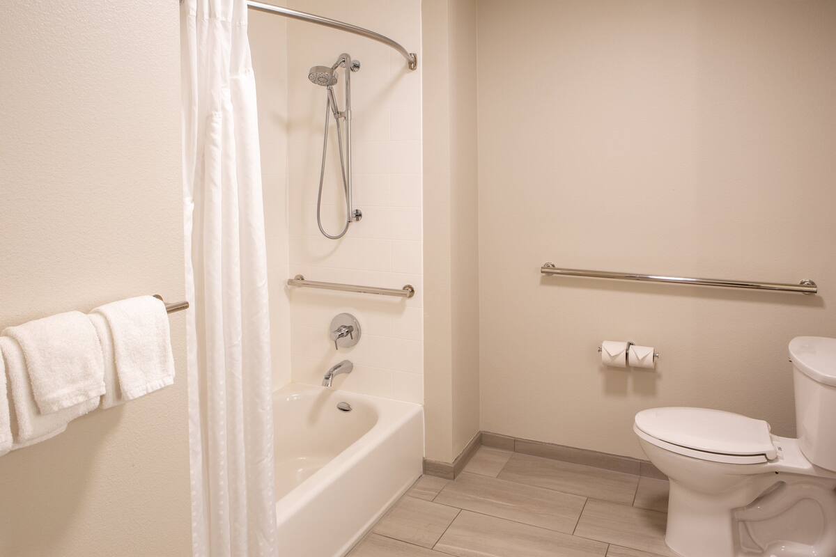 Une salle de bain équipée d’une baignoire, d’une douche, de toilettes et de barres d’appui.