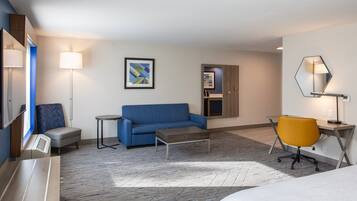 A modern hotel room with a blue sofa, a small table, a yellow chair, and a bed.