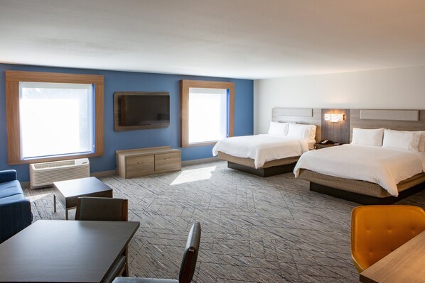 A hotel room with two beds, a desk, a chair, a TV, and a window.