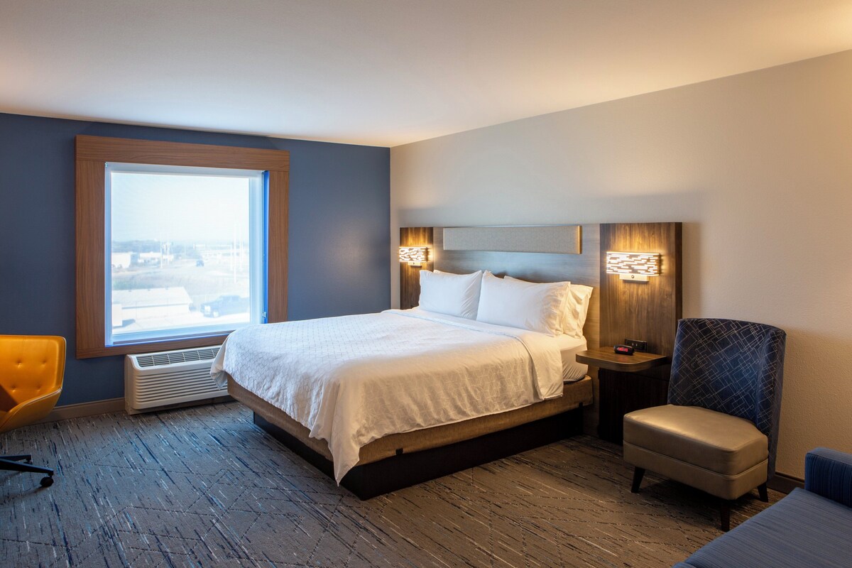Een hotelkamer met een groot bed, een stoel, een nachtkastje en een raam met uitzicht.