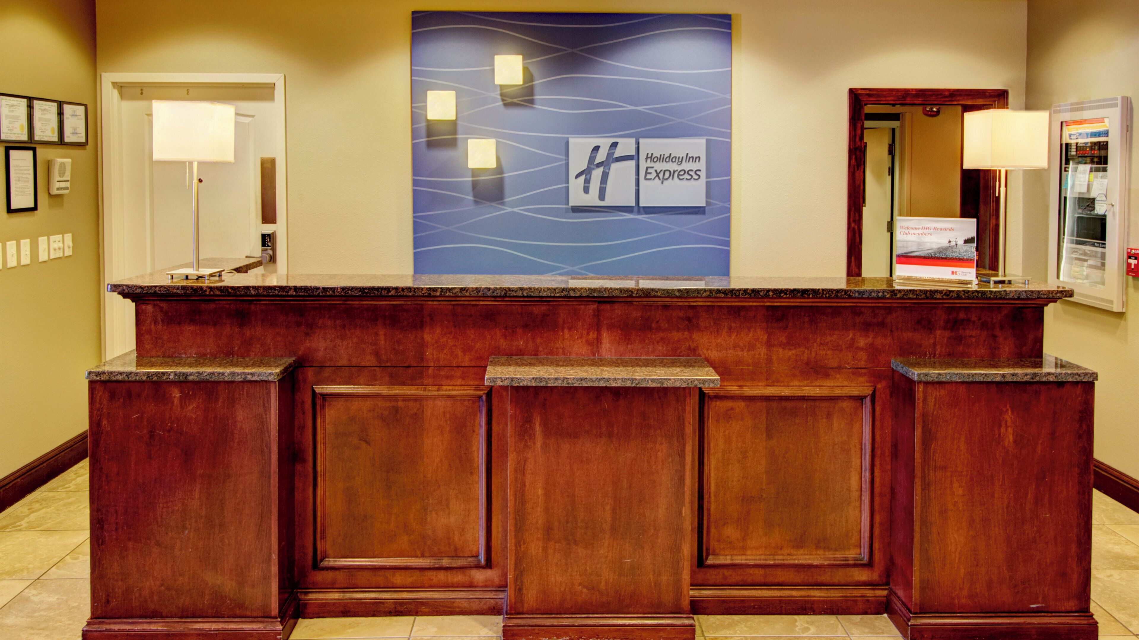 Un mostrador de recepción con el letrero de Holiday Inn Express, certificados enmarcados en la pared y una puerta a la izquierda.