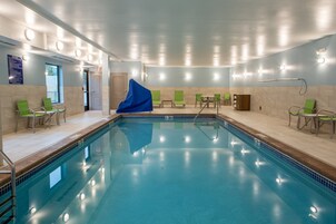 A large indoor swimming pool with multiple lounge chairs and a blue cover on the left side.