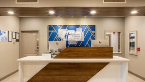 Un comptoir d’accueil agrémenté d’un motif géométrique bleu et blanc sur le mur, d’un élément décoratif en bois et d’une enseigne indiquant « Holiday Inn Express & Suites ».