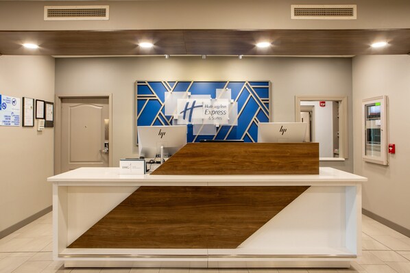 Un comptoir d’accueil agrémenté d’un motif géométrique bleu et blanc sur le mur, d’un élément décoratif en bois et d’une enseigne indiquant « Holiday Inn Express & Suites ».