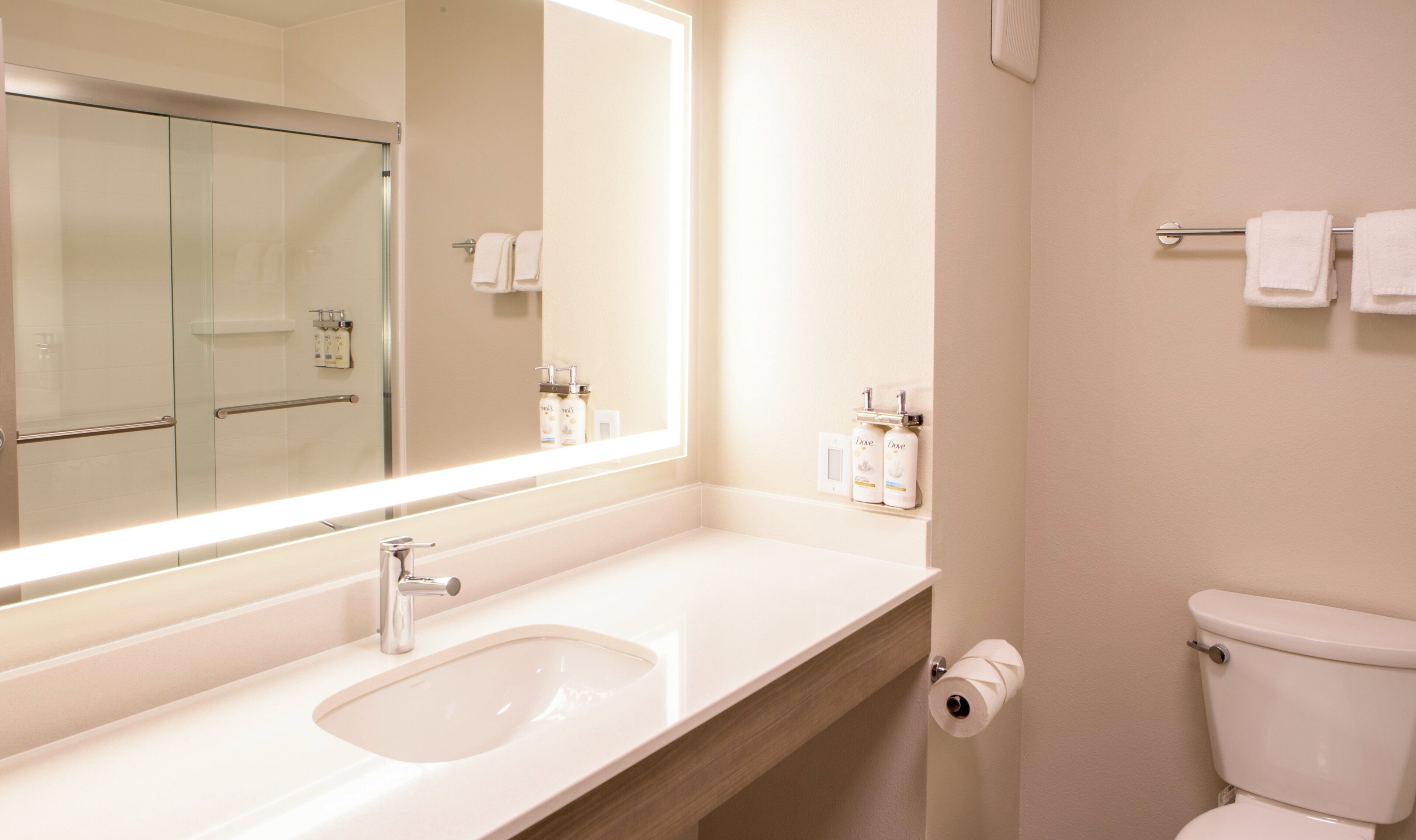 A bathroom with a large mirror, a sink, a toilet, and a towel rack.