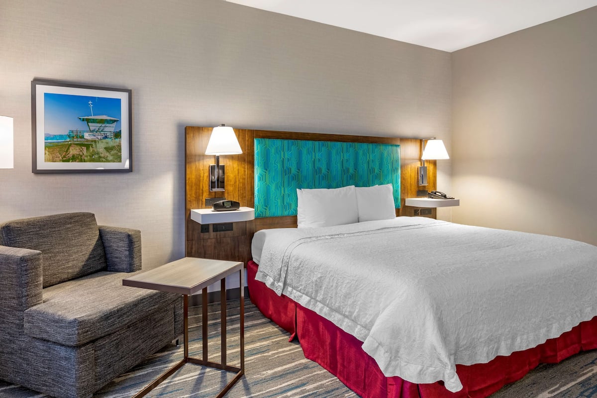 A hotel room with a bed, a chair, a small table, and a nightstand with lamps.