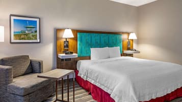 A hotel room with a bed, a chair, a small table, and a nightstand with lamps.