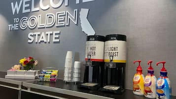 A reception area with a 'Welcome to the Golden State' sign, coffee dispensers, and condiments.
