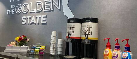 Un área de recepción con un cartel que dice 'Welcome to the Golden State', dispensadores de café y aderezos.