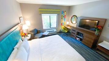 Une chambre d’hôtel avec un grand lit, un bureau, une chaise, une télévision et une fenêtre donnant sur la forêt.