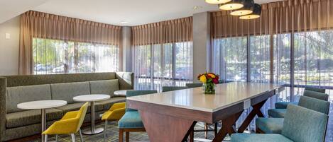 A modern hotel lobby with a large seating area, a central table, and large windows with curtains.