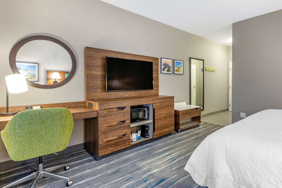 A hotel room with a large bed, a desk with a chair, a television, a microwave, and a coffee maker.