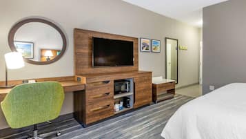 Habitación de hotel con una cama grande, un escritorio con silla, televisión, microondas y cafetera.