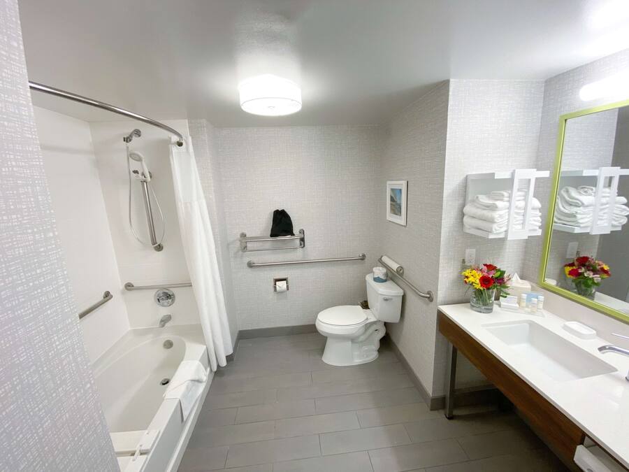 Un baño moderno con bañera, inodoro y lavamanos, equipado con barras de apoyo y un espejo.