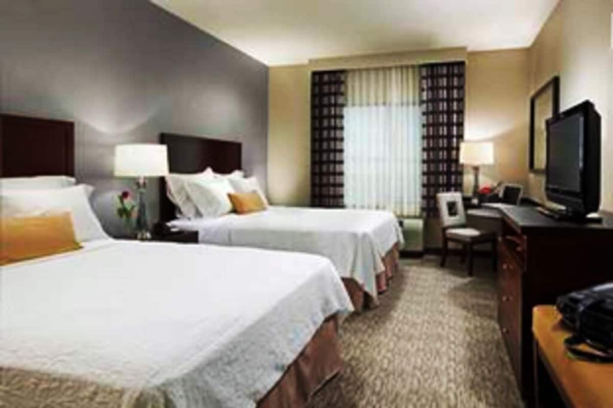 A hotel room with two beds, a desk, a television, and a window with curtains.
