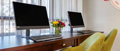 A wooden desk with two monitors, a keyboard, and a vase with flowers.