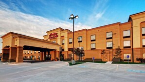 A Hampton Inn Suites hotel with a covered entrance, a parking lot, and a clear sky.