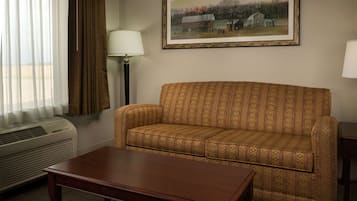 Una habitación con un sofá estampado, una mesa de centro de madera, un cuadro enmarcado en la pared y una ventana con cortinas.