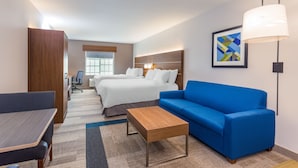 A hotel room with a bed, a blue sofa, a wooden coffee table, a desk, and a lamp.