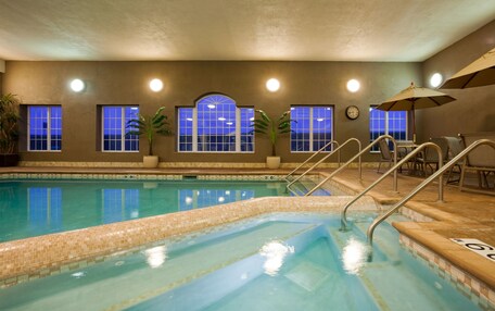 An indoor swimming pool with clear blue water, tiled steps, and a clock on the wall.