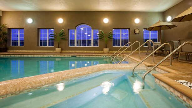An indoor swimming pool with clear blue water, tiled steps, and a clock on the wall.