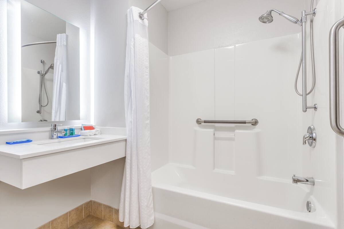 Un baño moderno con lavamanos, espejo y bañera blancos.