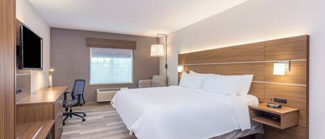 A hotel room with a bed, desk, chair, and a TV.