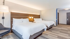 A hotel room with two beds, a desk, a chair, and a lamp.