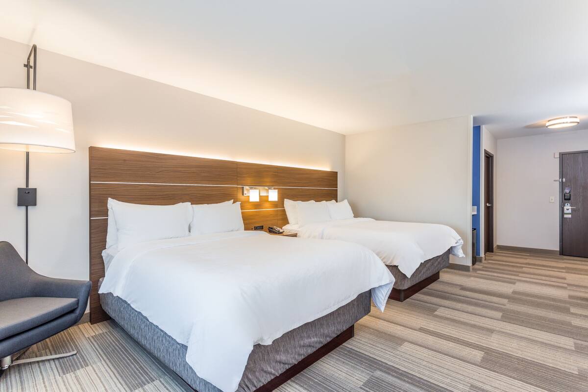 Una habitación de hotel con dos camas, un escritorio, una silla y una lámpara.