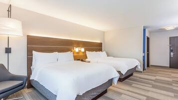 A hotel room with two beds, a desk, a chair, and a lamp.