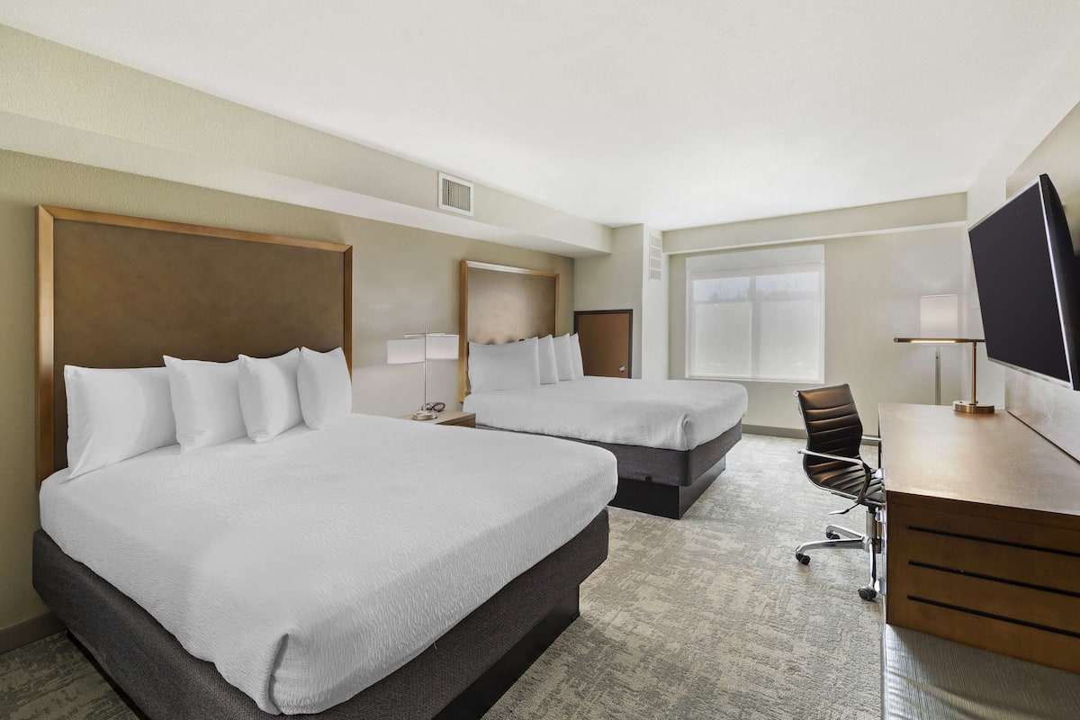 A hotel room with two beds, a desk, a chair, and a television.