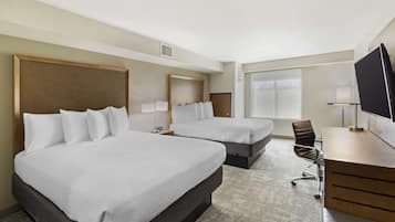 A hotel room with two beds, a desk, a chair, and a television.