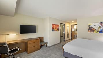 Une chambre d’hôtel comprenant un lit, un bureau avec une chaise, un téléviseur à écran plat, un petit banc et des œuvres d’art accrochées aux murs.
