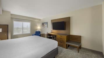 A hotel room with a large bed, a desk with a chair, a television mounted on the wall, and a window providing a view of the outside.