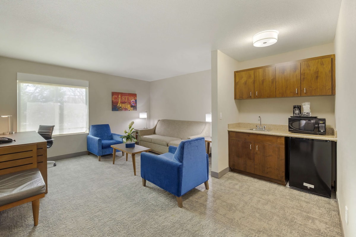 A living room with a blue sofa, a wooden dining table, and a kitchen area with wooden cabinets and a microwave.