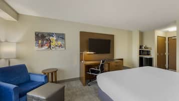 Habitación de hotel con cama, sofá azul, escritorio con silla, televisor y un cuadro en la pared.