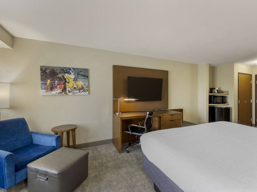 A hotel room with a bed, a blue sofa, a desk with a chair, a TV, and a painting on the wall.