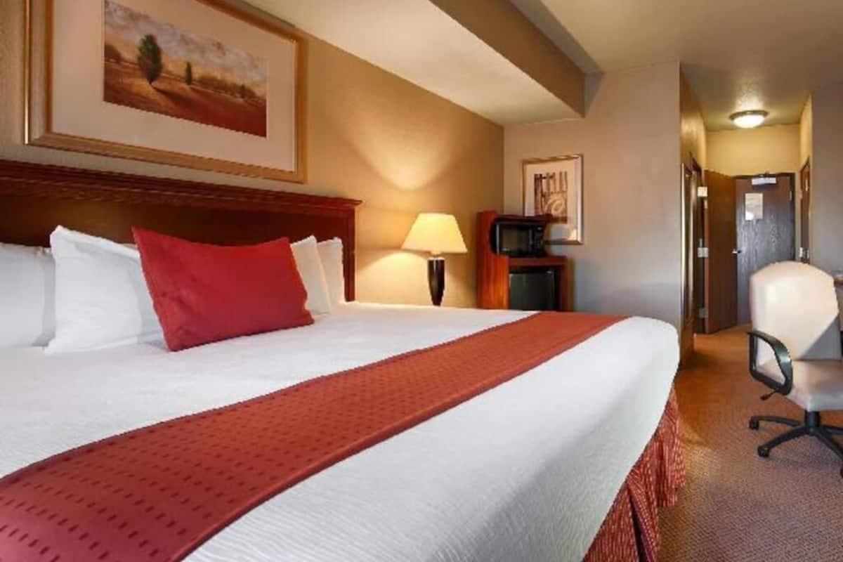 A hotel room with a large bed, a desk, a chair, and a television.